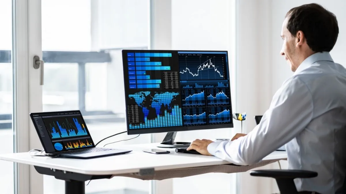 Business analyst reviewing industry research and workflow performance dashboards on multiple screens.